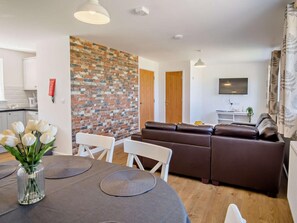 Ein modernes Wohnzimmer mit einer Ziegelwand, einem braunen Ledersofa, einem Esstisch mit Untersetzern und einer Vase mit weißen Blumen.