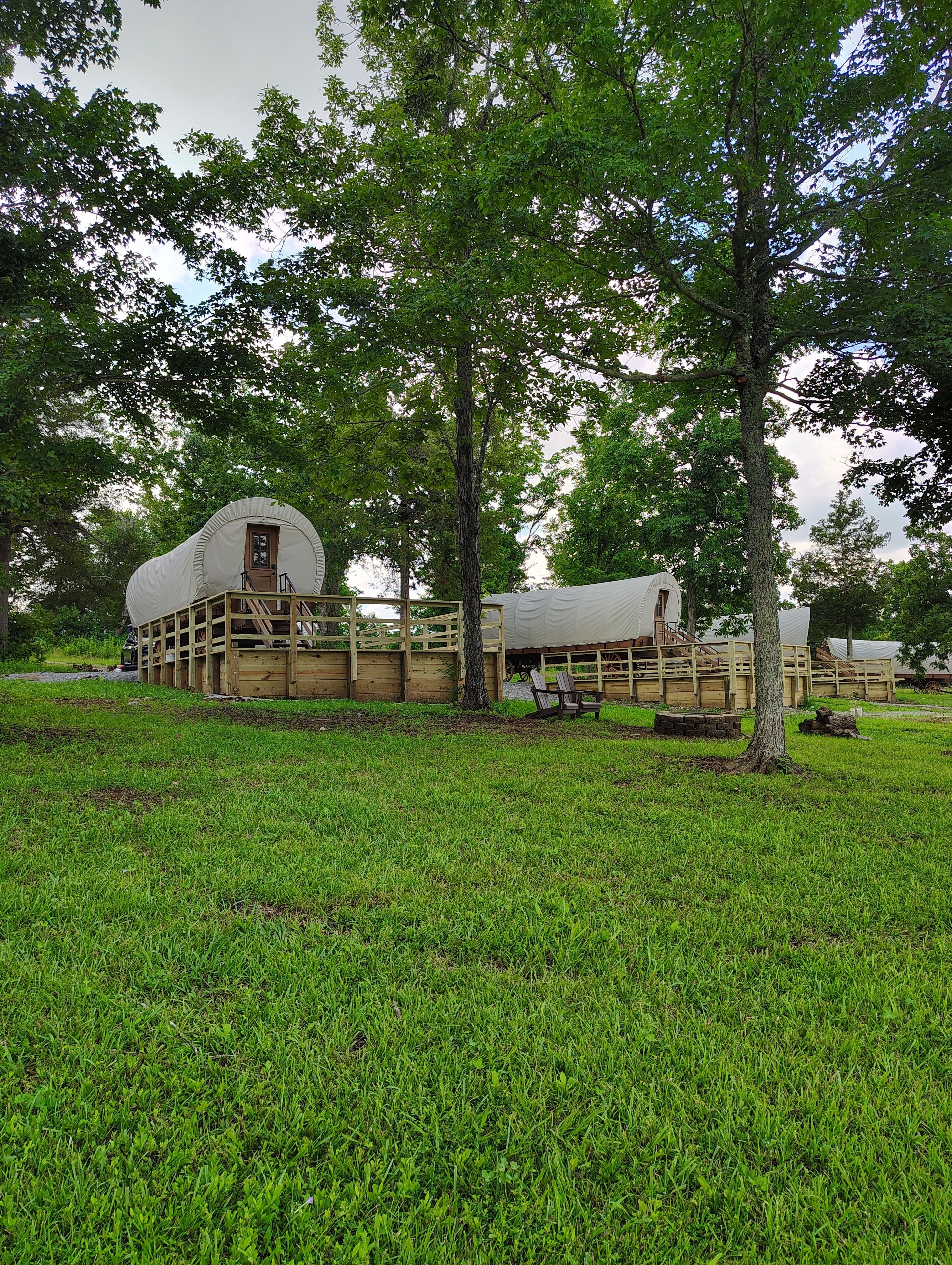 A covered structure with a wooden deck and a door, surrounded by trees and grass.