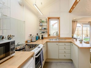 Eine kompakte Küche mit Mikrowelle, Herd, Spüle und einem Fenster mit Blick auf den Garten.