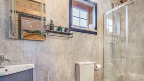 Ein Badezimmer mit Toilette, Waschbecken, Dusche und einem Fenster über der Toilette.