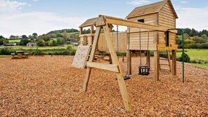Eine Holzspielanlage mit Schaukel und Kletterwand, eingebettet in eine Mulchschicht.