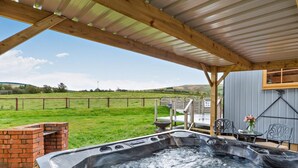 Ein Whirlpool unter einer Hollaube, mit einem grünen Feld und Hügeln im Hintergrund.