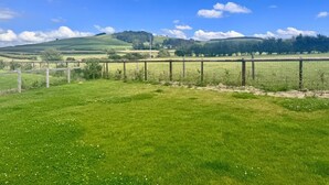 Paesaggio rurale con dolci colline, una recinzione e un cielo azzurro limpido.