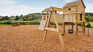 Una struttura giochi in legno con scivolo e parete da arrampicata, circondata da un’area con pietrisco.