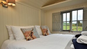 Una camera da letto con un letto grande, due cuscini con fantasie animalier, una finestra vista sul verde e una lampada a parete.