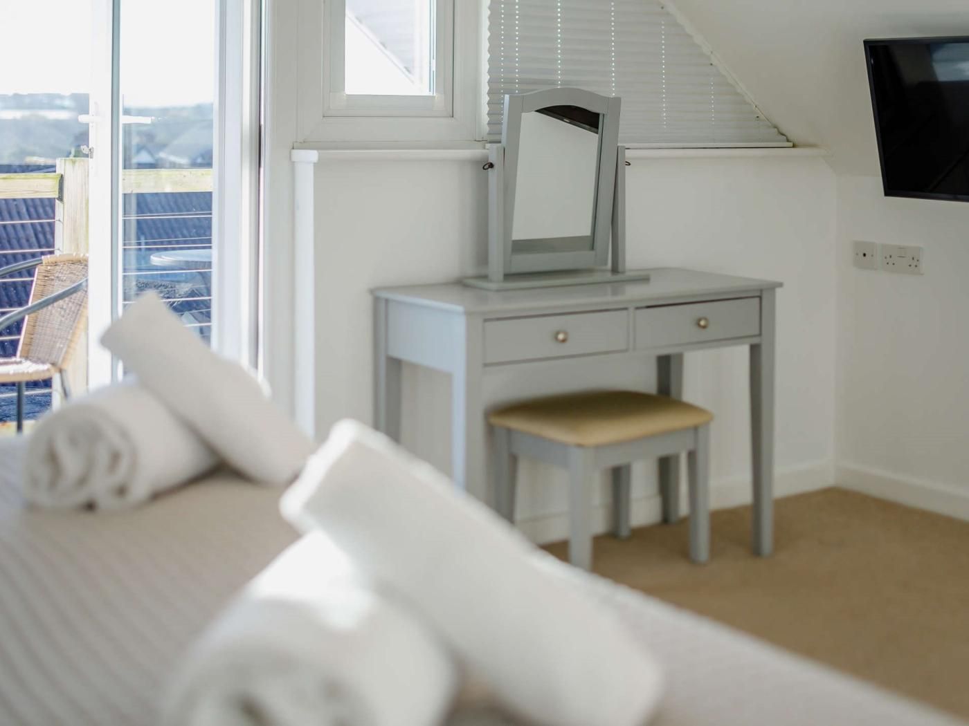 Un dormitorio con cama, mesita de noche con espejo, una silla y vistas al exterior.