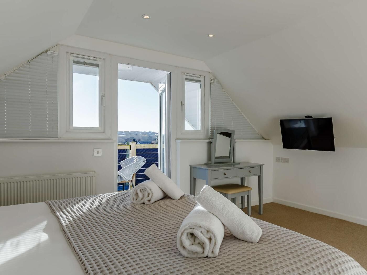 A bedroom with a bed, a desk, a television, and a view of the sea.