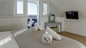 Ein Schlafzimmer mit einem Bett, einem Schreibtisch, einem Fernseher und Blick aufs Meer.