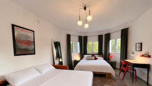 A hotel room with two beds, a desk, a chair, a mirror, a poster, and a patterned rug.