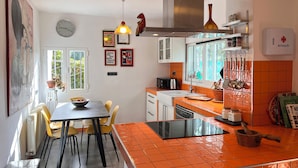 A kitchen with a dining area, a clock, and various kitchen utensils.
