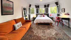 A bedroom with a bed, a desk, a red chair, a brown sofa, and a patterned rug.