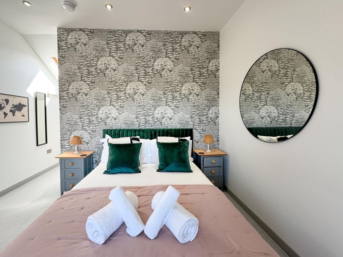 A bedroom with a large bed, two nightstands, a round mirror, and a patterned wallpaper.