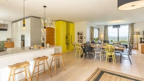 Una cocina moderna con una isla central, un comedor con sillas amarillas y vistas al exterior.