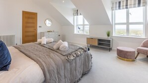 Un dormitorio con una cama, un aparador, una tocador, un espejo redondo, una ventana con vistas y una lámpara colgante.