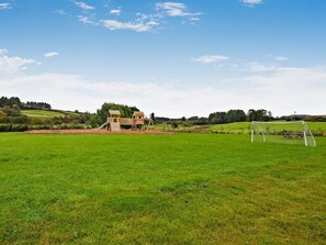 Ein Spielplatz mit Rutsche und Klettergerüsten, umgeben von einer Wiese und Bäumen.