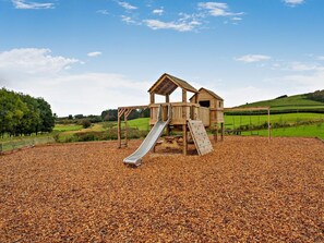 Eine Holz-Spielanlage mit Rutsche und Kletterwand, umgeben von einem Kiesplatz.