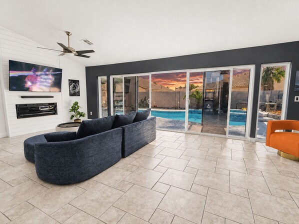 A modern living room with a sectional sofa, a flat-screen TV, and a sliding glass door leading to a pool area.