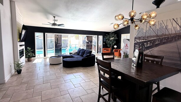 A spacious living area with a dark-colored sofa, a dining table with chairs, a ceiling fan, and a view of a swimming pool through glass doors.
