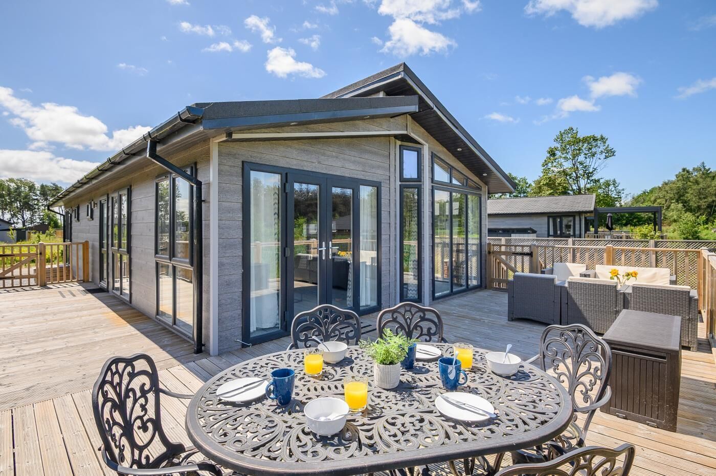 Ein zeitgemäßer Essbereich im Freien mit einem Tisch für zwei Personen, umgeben von Stühlen, und einer Terrasse, die zu einem Gebäude mit großen Glasfenstern führt.