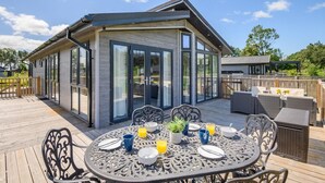 Ein zeitgemäßer Essbereich im Freien mit einem Tisch für zwei Personen, umgeben von Stühlen, und einer Terrasse, die zu einem Gebäude mit großen Glasfenstern führt.