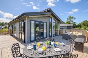 Ein zeitgemäßer Essbereich im Freien mit einem Tisch für zwei Personen, umgeben von Stühlen, und einer Terrasse, die zu einem Gebäude mit großen Glasfenstern führt.