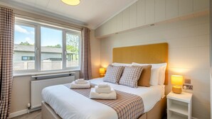 Ein Schlafzimmer mit einem großen Bett, zwei Nachttischlampen, einem Fenster mit Vorhängen und Blick nach draußen.