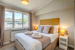 Ein Schlafzimmer mit einem großen Bett, zwei Nachttischlampen, einem Fenster mit Vorhängen und Blick nach draußen.