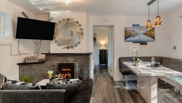 Ein modernes Wohnzimmer mit Kamin, einem Wand-Fernseher und einem Essbereich mit Pendelleuchten.