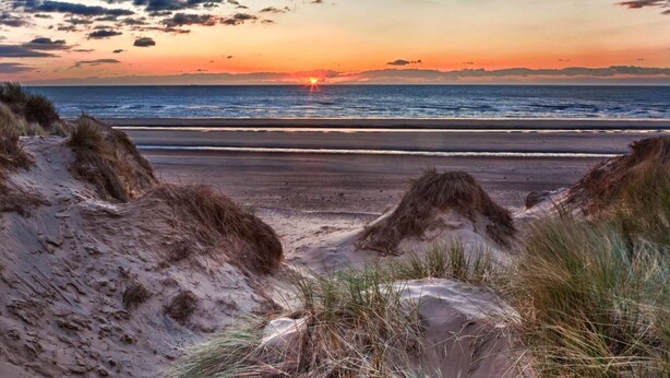 Ein Strand mit Dünen und einem Sonnenuntergang über dem Meer.