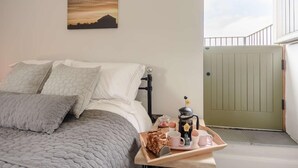 Ein Schlafzimmer mit Bett, Kissen, einem Nachttisch mit Frühstücksgedecken, einem Wandbild und Blick auf einen Balkon.