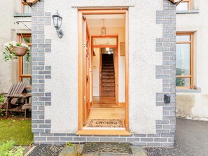 A building entrance with a wooden door, a doormat, and a hanging basket. - 3 Bed in Corwen (oc-90459) (Corwen)