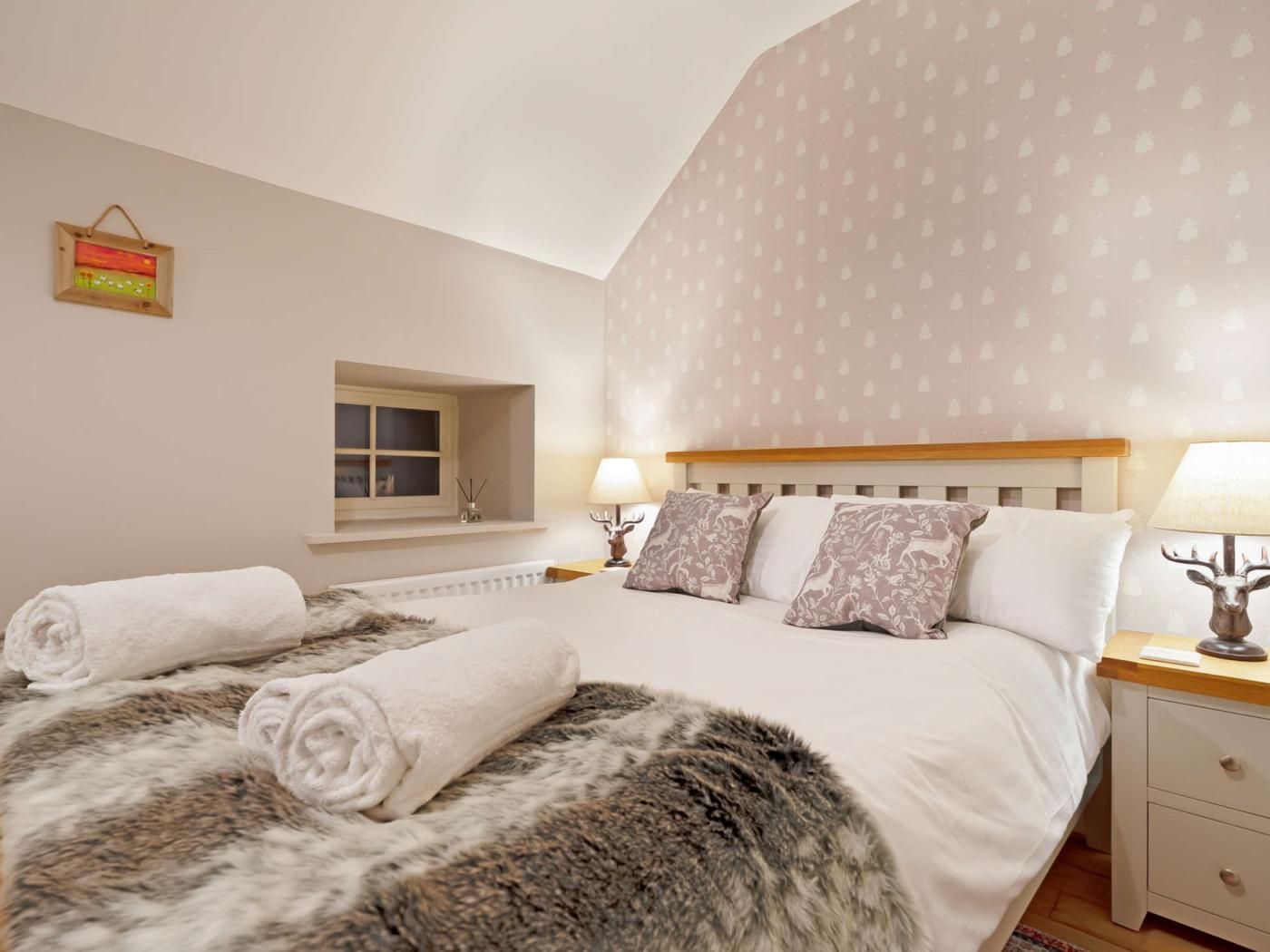 Une chambre à coucher avec un grand lit, deux lampes de chevet, une fenêtre et un tableau accroché au mur.