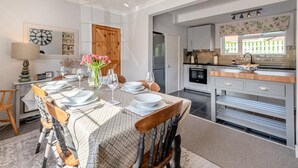 A dining area with a table set for four, a kitchen with modern appliances, and a large window with a view. - 3 Bed in Belford (oc-90351) (Belford)