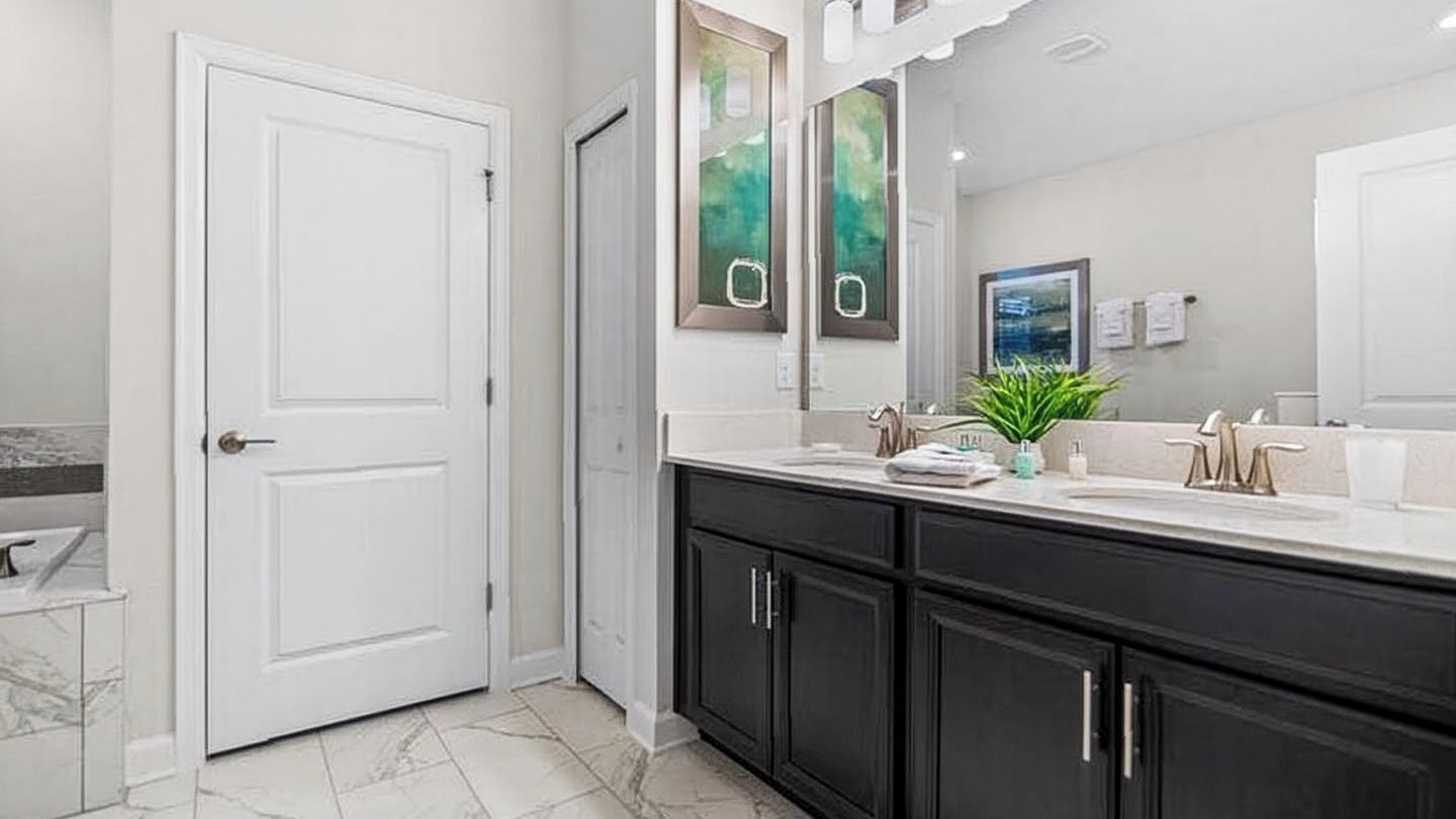 A bathroom with a white door, dark cabinets, a white countertop, a mirror, and a potted plant.