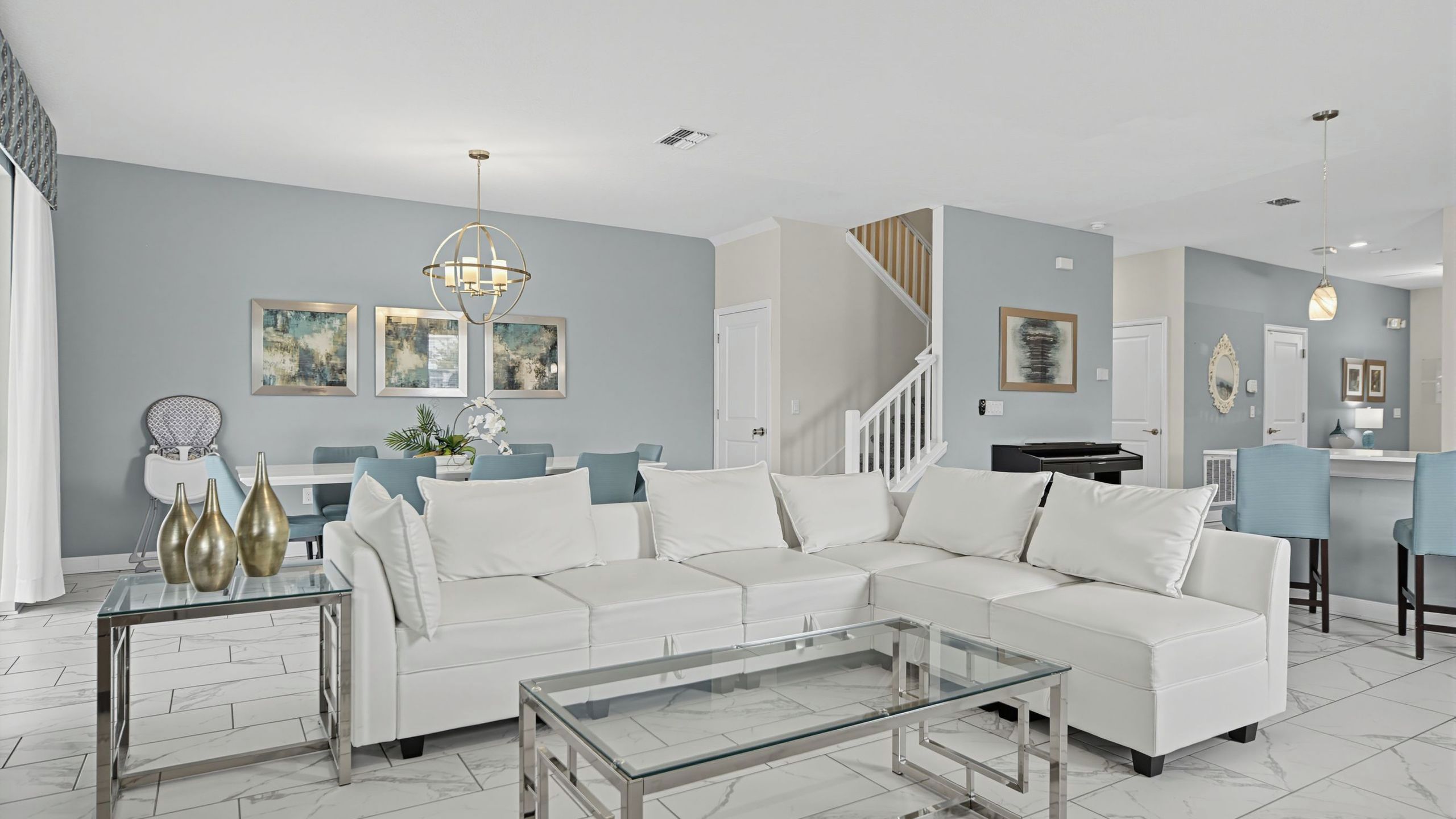 A modern living room with a white sectional sofa, a glass coffee table, and a dining area with a piano.