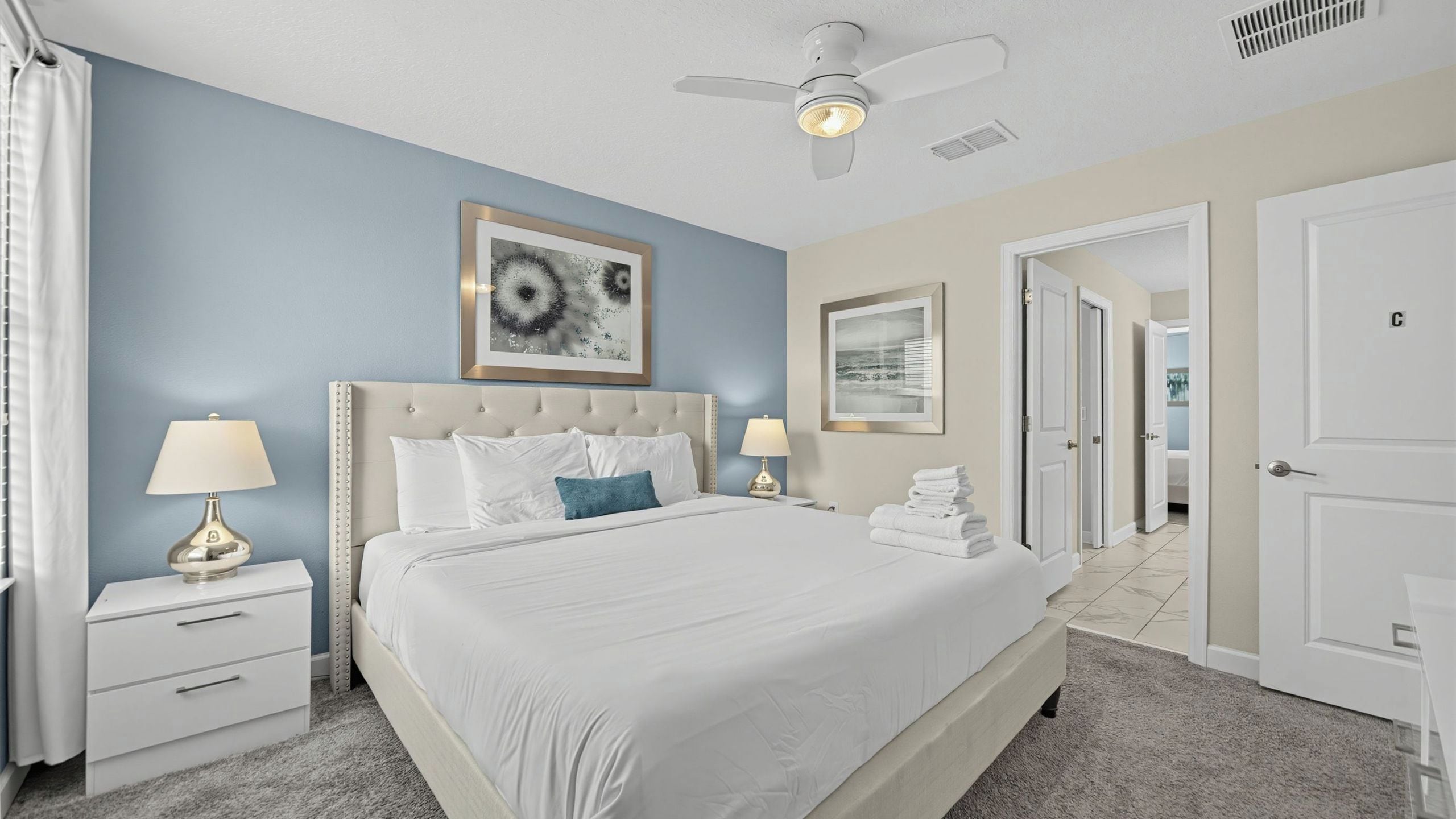 A hotel room with a bed, bedside tables, a ceiling fan, and artwork on the walls.