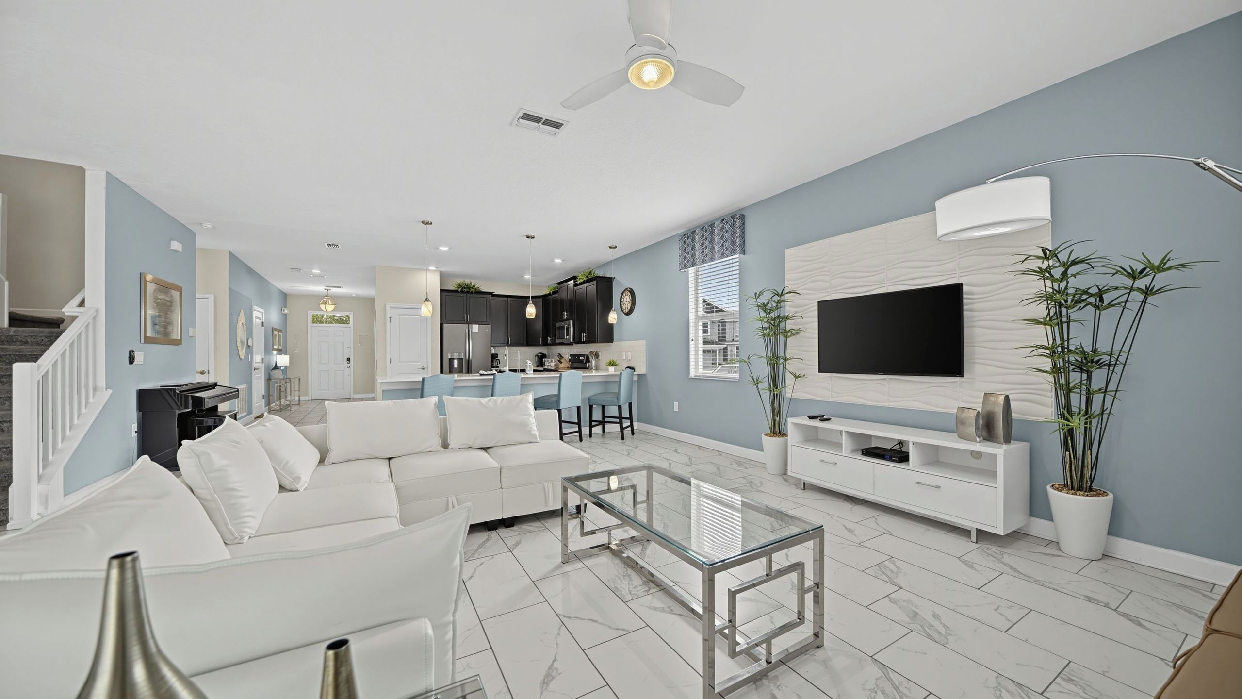 A modern living room with a white sofa, a glass coffee table, and a TV on a white wall.