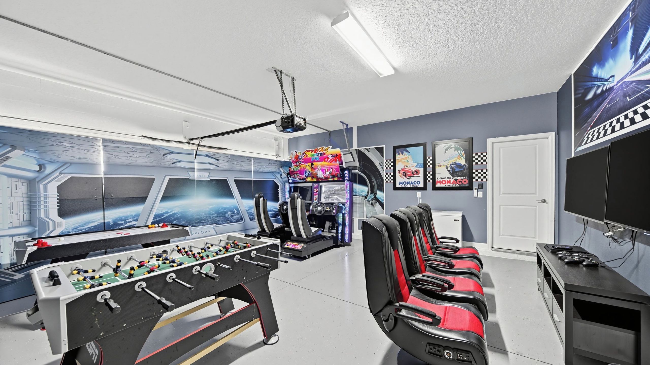 A room with a foosball table, racing posters, and a large window with a view of Earth.
