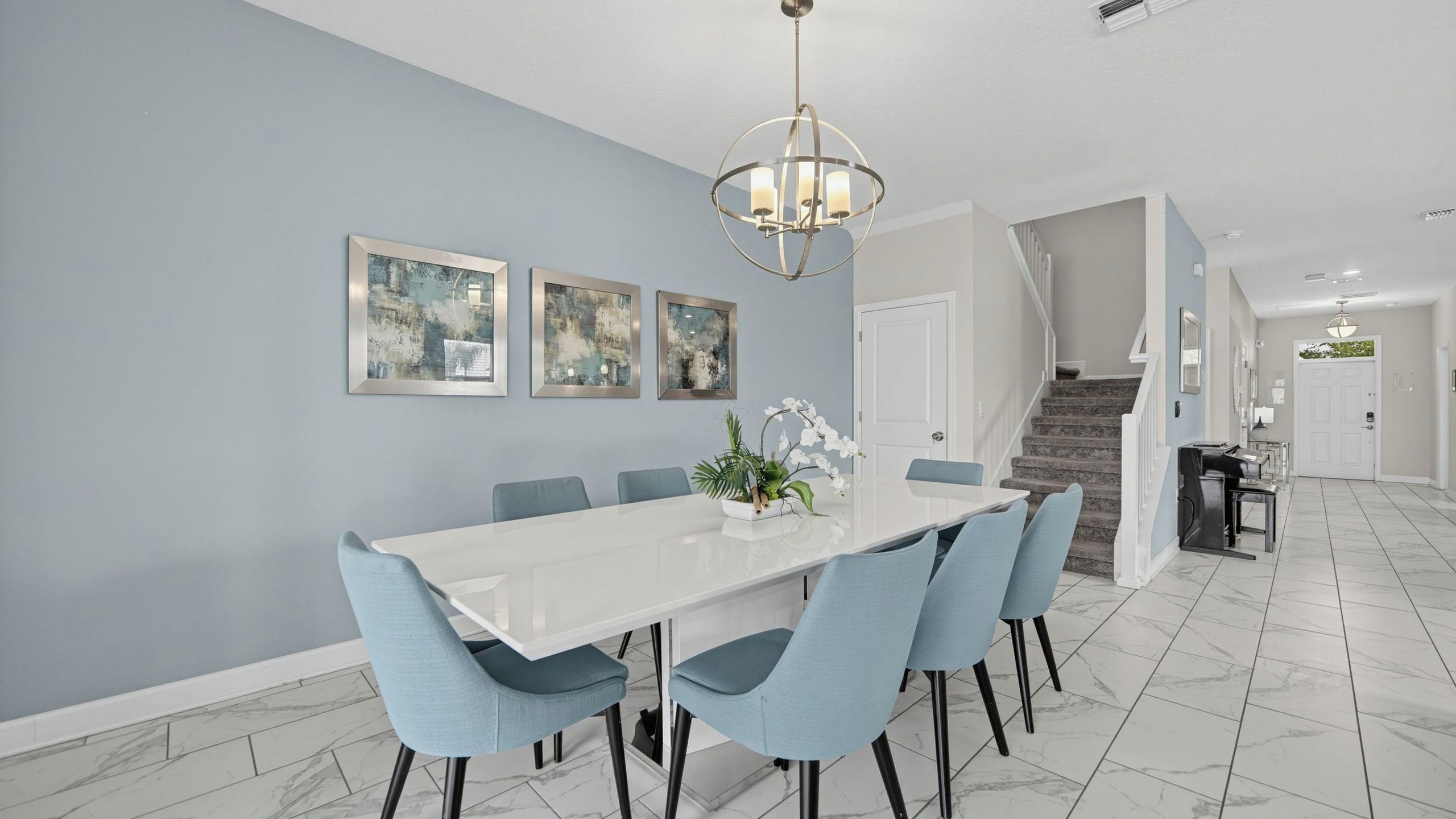 A dining area with a white table and blue chairs, a chandelier, and abstract art on the wall.
