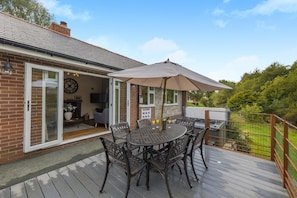 A patio with a table and chairs, a large umbrella, and a brick house with a glass door. - 3 Bed in Rhayader (oc-90282) (Saint Harmon)