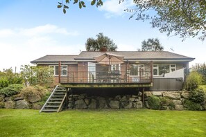 Una casa a due piani con una veranda, una scalinata che porta alla veranda e un muro in pietra sullo sfondo.