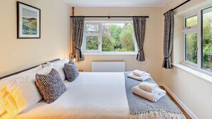 Une chambre à coucher avec un lit, une fenêtre avec des rideaux, un radiateur, un luminaire suspendu et un tableau encadré au mur.
