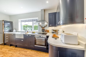 A modern kitchen with dark cabinetry, a built-in oven, a microwave, and a toaster. - 3 Bed in Rhayader (oc-90282) (Saint Harmon)