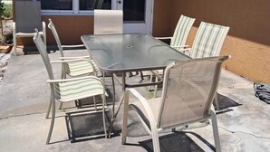 Eine Terrasse mit Tisch und Stühlen, eine Glasschiebetür und ein kleiner überdachter Bereich.
