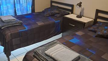 A bedroom with two beds, a nightstand with a lamp, and a window with curtains.
