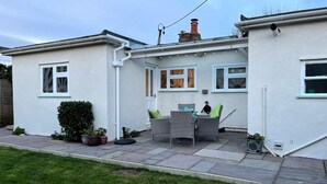 Uma casa de dois andares com um pátio, uma chaminé e um pequeno jardim.