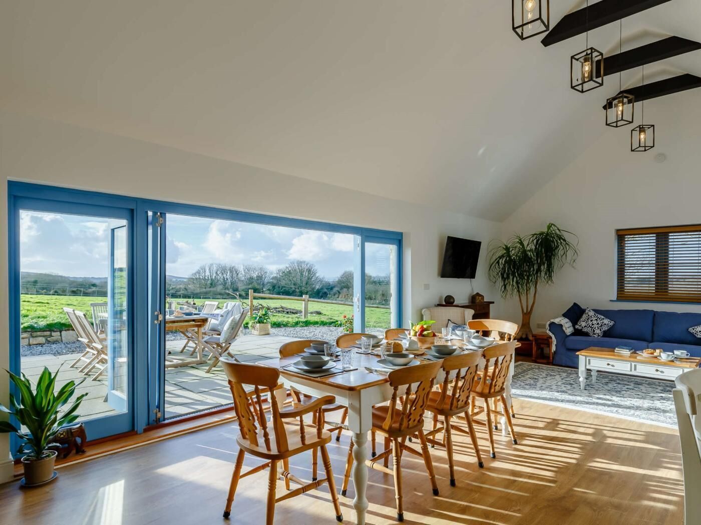 A dining area with a table set for four, a sofa, a TV, and a large window with a view of a green landscape.