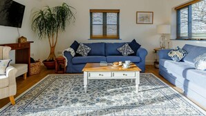 En stue med en blå sofa, et sofabord, en potteplante og et fjernsyn monteret på væggen.