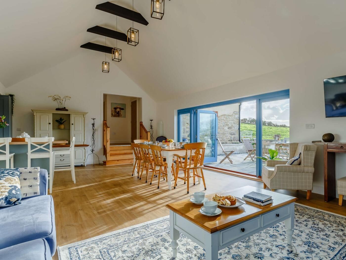 A spacious living area with a dining table, chairs, a sofa, and a coffee table. There is a view through a glass door to an outdoor area.