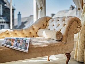 A tufted sofa with a newspaper, positioned near a window with a view of buildings. - 6 Bed in Keswick (oc-90333) (Keswick)